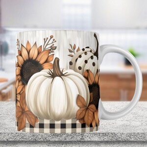 May include: White ceramic mug with a fall-themed design. The mug features a white pumpkin with brown stems, sunflowers, and a black and white checkered pattern.