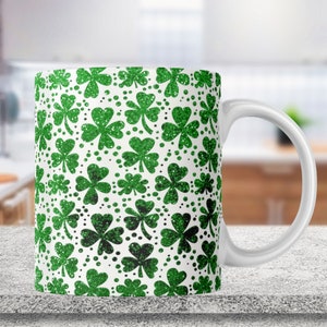 Könnte beinhalten: Weiße Keramiktasse mit einem grünen Kleeblatt-Muster. Die Kleeblätter sind mit Glitzer bedeckt.