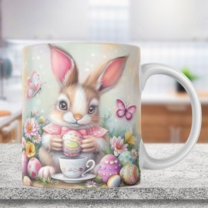 May include: White ceramic mug with a colorful illustration of an Easter bunny holding a decorated egg. The bunny is surrounded by flowers and butterflies. The mug has a handle.