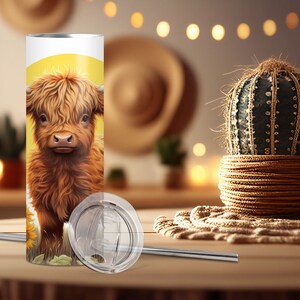 Puede incluir: Un vaso de acero inoxidable con una ilustraci&oacute;n de una vaca de las Tierras Altas sobre un fondo amarillo. El vaso incluye una tapa y una pajita de metal. El dise&ntilde;o muestra una vaca marr&oacute;n y beige con un girasol.