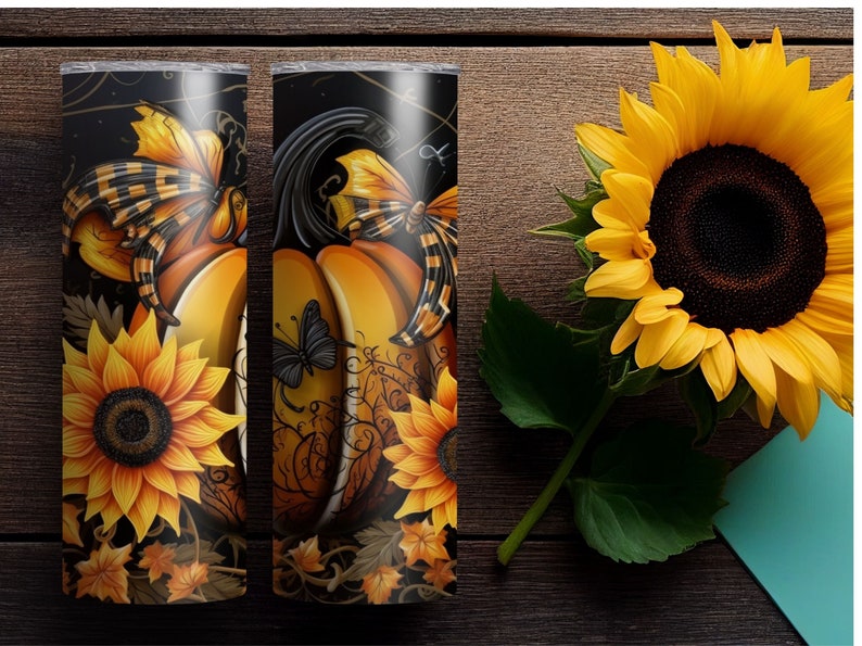 May include: Two 20 oz. stainless steel tumblers with a fall-themed design. The design features pumpkins, sunflowers, and butterflies in shades of orange, yellow, and black. The tumblers are set against a dark background.