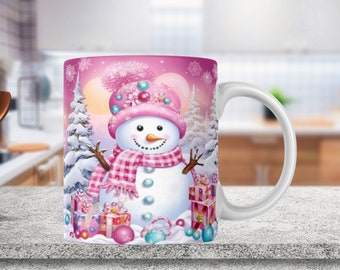May include: A white ceramic mug with a pink handle features a festive snowman design. The snowman is wearing a pink hat with a white pom-pom and a pink and white plaid scarf. The background is a pink and white winter scene with snow-covered trees and presents.