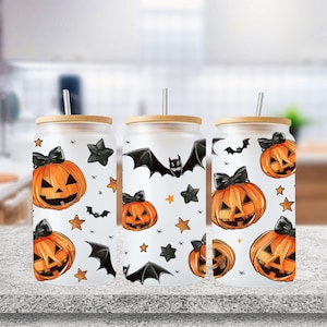 May include: Three white tumblers with a Halloween theme. Each tumbler features a black and orange pumpkin with a spooky face, bats, and stars. The tumblers have a bamboo lid and straw.