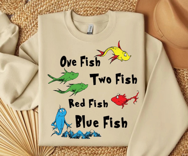 May include: A beige sweatshirt with a graphic of four fish and the text "One Fish Two Fish Red Fish Blue Fish".