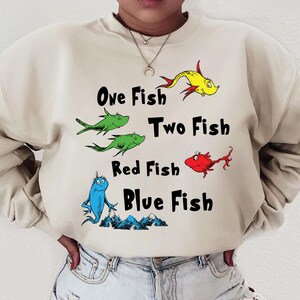 May include: A beige sweatshirt with a graphic print of fish and the text "One Fish Two Fish Red Fish Blue Fish".