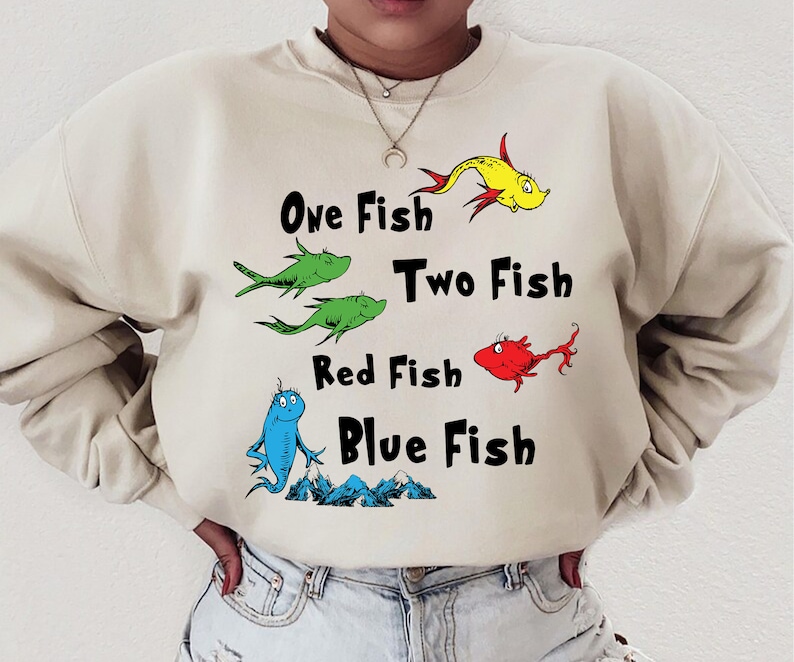 May include: A beige sweatshirt with a graphic print of fish and the text "One Fish Two Fish Red Fish Blue Fish".