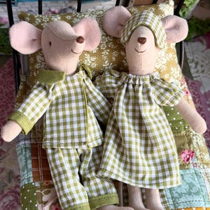 Op de afbeelding: Twee pluche muispoppen in een miniatuurbed. Eén muis draagt een groen-witte geruite pyjama, de andere een bijpassende nachtjapon en slaapmasker. Het bed heeft een kussen met bloemenpatroon en een patchworkquilt.