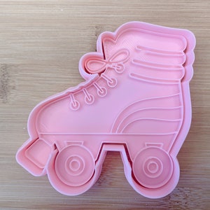 May include: Pink plastic roller skate cookie cutter. The cutter is shaped like a classic roller skate with four wheels and a lace-up design.
