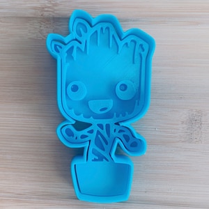 May include: A blue plastic cookie cutter shaped like a cartoon character, Groot from Guardians of the Galaxy, standing in a pot.