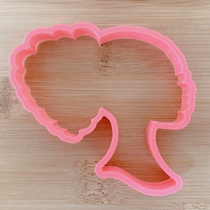 May include: Pink plastic cookie cutter shaped like a woman with an afro hairstyle.