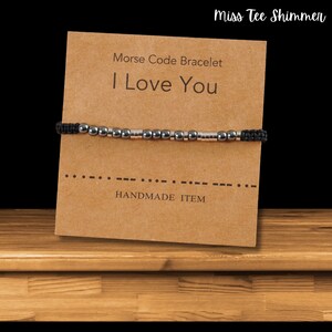 May include: A black and silver beaded bracelet with a brown card that reads "Morse Code Bracelet I Love You" and "Handmade Item".