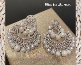 May include: A pair of silver earrings with a crescent moon design, featuring white pearls and clear rhinestones. The earrings are displayed in a box with the text "Miss Tee Shimmer".