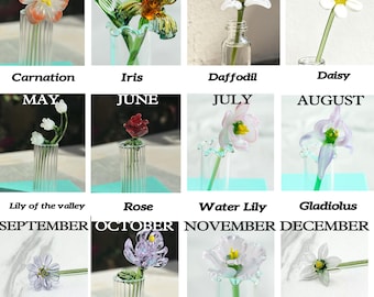 May include: A collection of glass flower sculptures, each representing a month of the year. The flowers include a carnation, iris, daffodil, daisy, lily of the valley, rose, water lily, gladiolus, aster, marigold, peony, and narcissus. Each flower is in a small glass vase.
