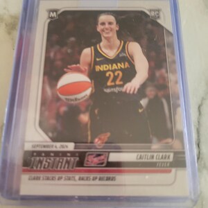 May include: A Caitlin Clark basketball card in a protective sleeve. The card features Clark in an Indiana Fever uniform, holding a basketball. The card is labeled "Instant" and includes the date "September 4, 2024."
