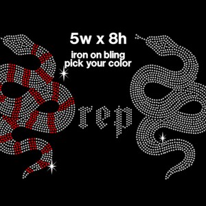 May include: Iron-on rhinestone design featuring two snakes, one with red and white stripes, the other in white. The design measures 5 inches wide by 8 inches high. The text "5w x 8h iron on bling pick your color" is also included.