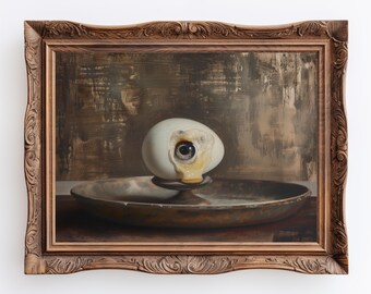 May include: A white egg with a human eye peering out of it, resting on a brown plate. The egg is cracked and dripping with yolk. The image is framed in a dark wood frame.
