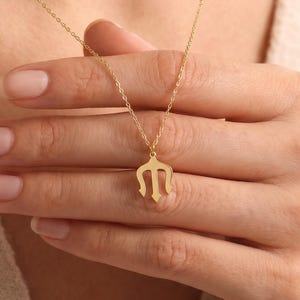 Pode incluir: Um colar de cor dourada com uma corrente delicada e um pequeno pendente em forma de tridente estilizado. O pendente tem três pontas e um ponto central, suspenso por uma corrente fina de metal dourado polido que repousa sobre o peito.