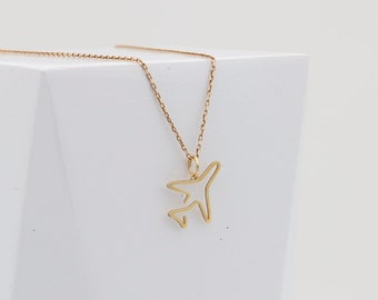 May include: A gold necklace with a delicate airplane pendant. The necklace is on a white background with a shadow of a plant.