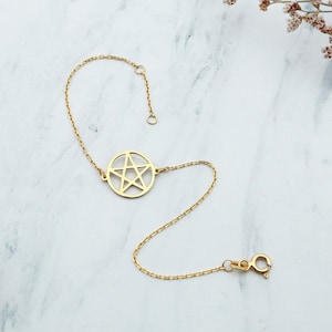 May include: A gold chain bracelet with a pentacle charm. The bracelet is on a white marble surface.