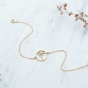 Op de afbeelding: Een gouden kettingarmband met een palmboom bedel. De bedel is een cirkel met een uitgesneden palmboom ontwerp.