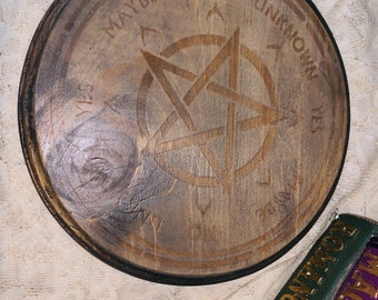 May include: A wooden Ouija board with a pentagram design and the words "Yes", "No", "Maybe", "Unknown" around the edge. A black pendulum is hanging from a chain.