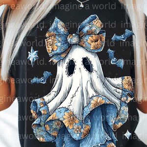May include: Black t-shirt featuring a whimsical ghost design. The ghost is adorned with a large blue bow and floral accents. Bats and stars surround the ghost, creating a spooky yet charming Halloween theme.