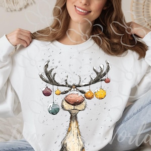 Puede incluir: Sudadera blanca con un dise&ntilde;o caprichoso de reno. El reno tiene grandes cuernos adornados con adornos coloridos. La ilustraci&oacute;n es de estilo caricaturesco, perfecta para la temporada navide&ntilde;a.