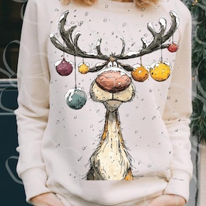 Puede incluir: Sudadera de color crema con un dise&ntilde;o caprichoso de reno. El reno tiene grandes cuernos adornados con adornos coloridos. Los copos de nieve est&aacute;n esparcidos alrededor del reno. Es una prenda festiva para las fiestas.