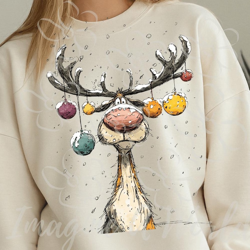 Puede incluir: Sudadera color crema con un dise&ntilde;o caprichoso de reno de dibujos animados. El reno tiene grandes astas adornadas con adornos coloridos y una prominente nariz roja. Los copos de nieve est&aacute;n esparcidos alrededor del reno, creando una escena invernal festiva.