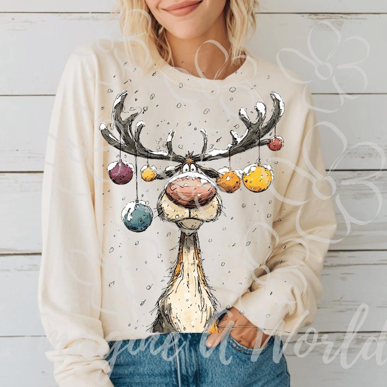 Puede incluir: Camiseta de manga larga color crema con un dise&ntilde;o caprichoso de un reno de dibujos animados. El reno tiene grandes cuernos adornados con adornos coloridos. Los copos de nieve est&aacute;n esparcidos alrededor del reno. Una prenda festiva y acogedora.