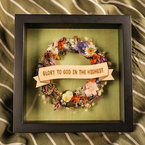 May include: A framed wreath made of dried flowers with a wooden banner that reads "Glory to God in the Highest".