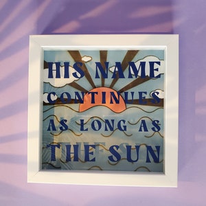 May include: White framed artwork with a blue and orange sunset scene and the text "HIS NAME CONTINUES AS LONG AS THE SUN".