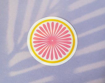 May include: A pink and yellow circular sticker with a stylized flower design. The flower has a pink center and yellow outline.
