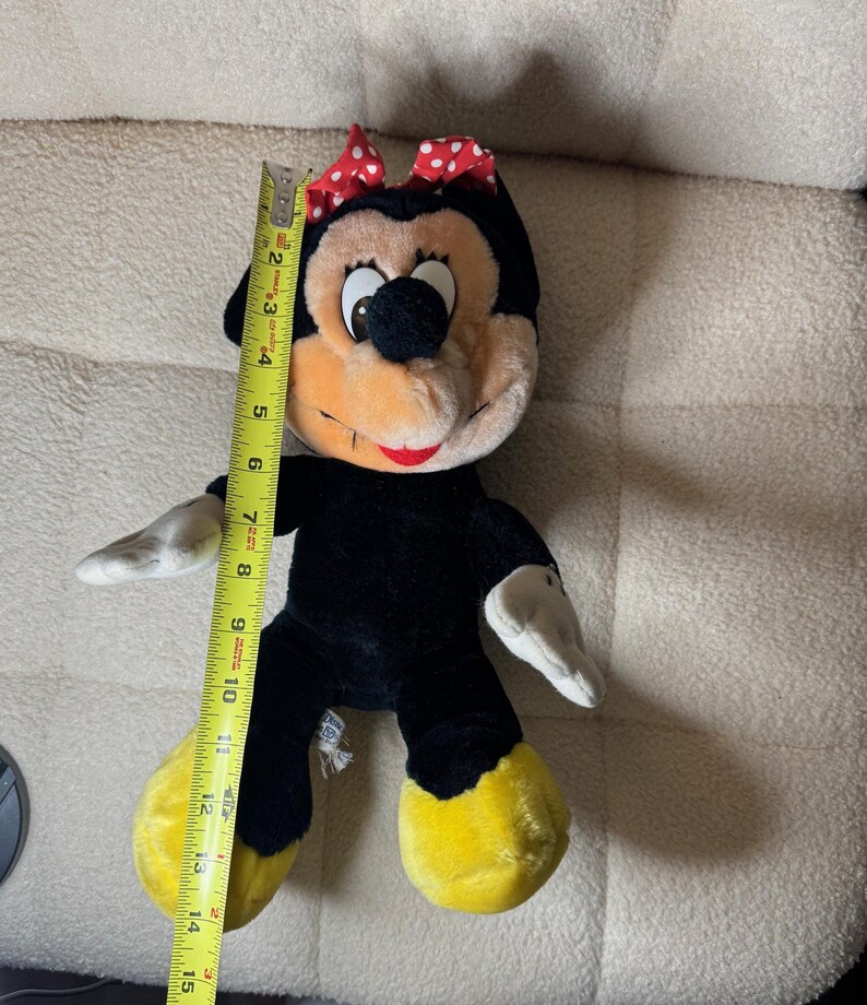 Puede incluir: Mu&ntilde;eca de peluche de Minnie Mouse, de aproximadamente 38 cm de altura, con cuerpo negro, pies amarillos y guantes blancos. Tiene un lazo rojo con lunares blancos y una cara sonriente con boca roja. La mu&ntilde;eca es de tela suave.