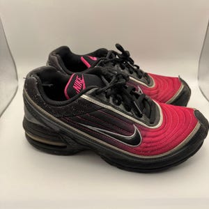 May include: Pair of black and pink athletic shoes with the Nike logo. The shoes have a black sole, pink accents, and a silver swoosh. The uppers are a gradient of pink to black.