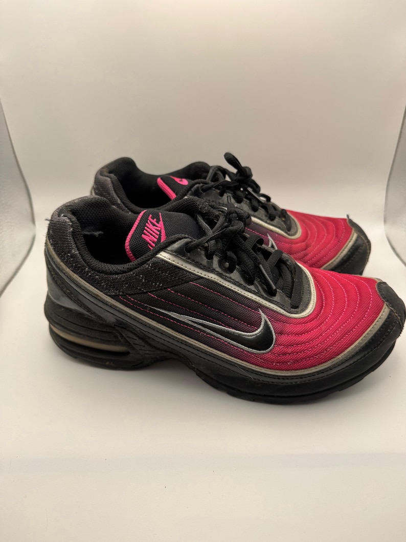 May include: Pair of black and pink athletic shoes with the Nike logo. The shoes have a black sole, pink accents, and a silver swoosh. The uppers are a gradient of pink to black.
