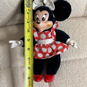 May include: A Minnie Mouse plush doll, approximately 10 inches tall, with black fur, a red and white polka dot dress, and a white bow. The doll has red shoes and white gloves. The doll is a vintage collectible.