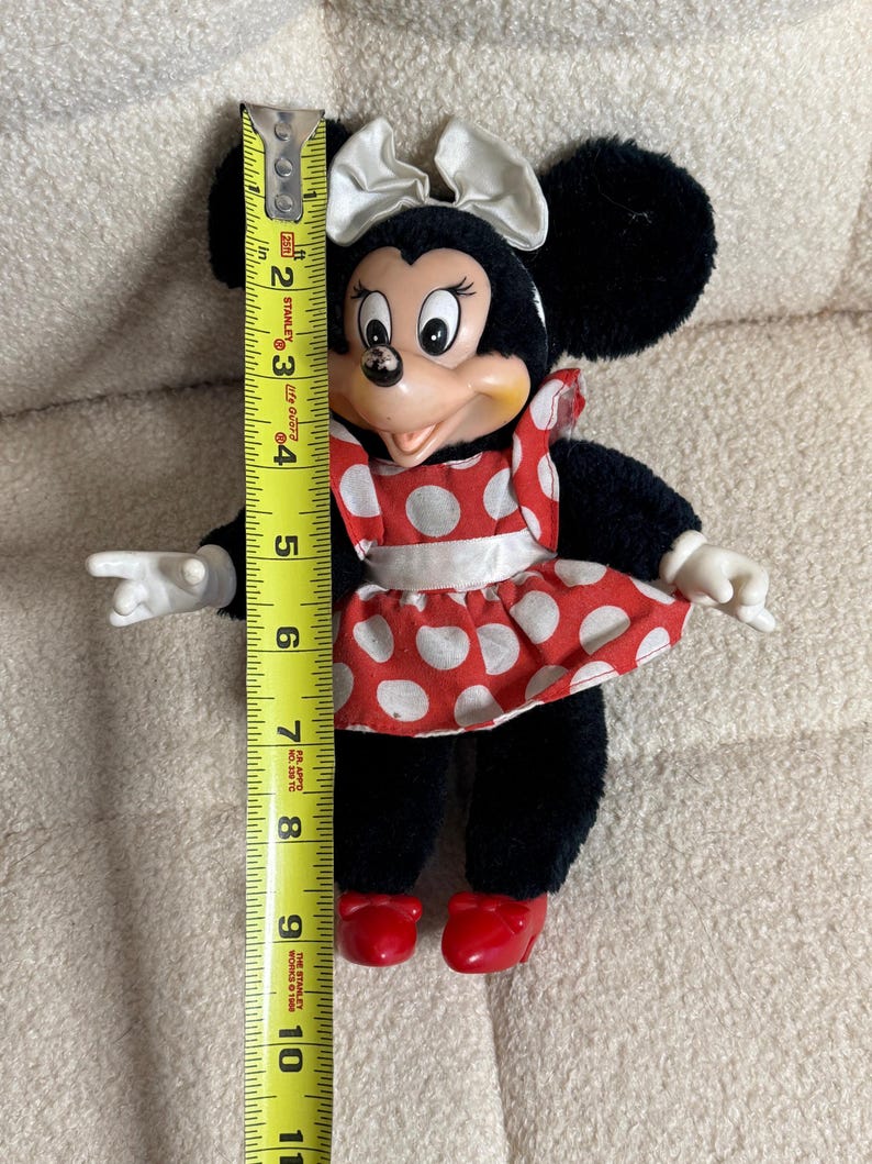 May include: A Minnie Mouse plush doll, approximately 10 inches tall, with black fur, a red and white polka dot dress, and a white bow. The doll has red shoes and white gloves. The doll is a vintage collectible.
