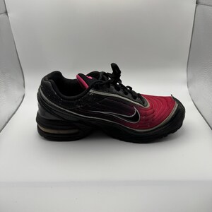 May include: Black and red athletic shoe with a black swoosh logo. The shoe has a pink accent on the tongue and a black sole. The shoe appears to be made of a combination of mesh and synthetic materials.