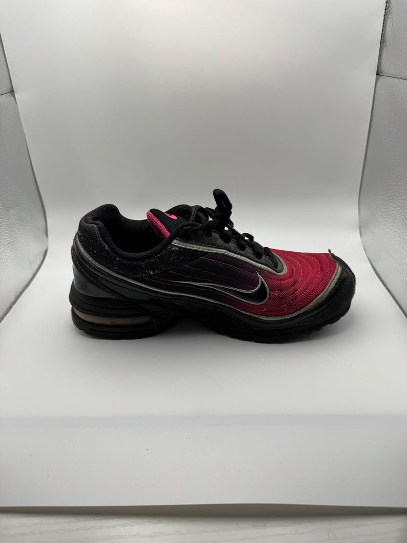 May include: Black and red athletic shoe with a black swoosh logo. The shoe has a pink accent on the tongue and a black sole. The shoe appears to be made of a combination of mesh and synthetic materials.