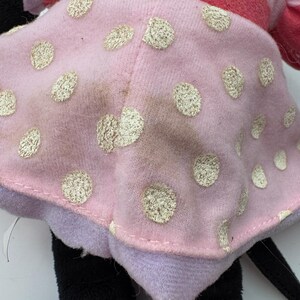 May include: A plush doll featuring a pink dress with gold polka dots. The doll has a red and pink striped top, black legs, and a black tail. The doll's dress has some discoloration.