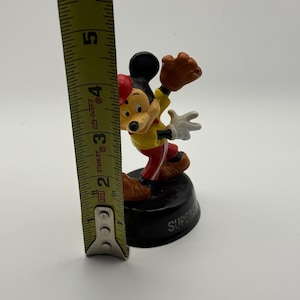 K&ouml;nnte beinhalten: Eine Mickey Mouse-Figur in Baseball-Uniform, etwa 7,6 cm hoch. Die Figur steht auf einem schwarzen Sockel mit dem Wort "SUPER". Mickey tr&auml;gt ein gelbes Hemd, eine rote Hose, eine rote M&uuml;tze und einen braunen Baseballhandschuh.