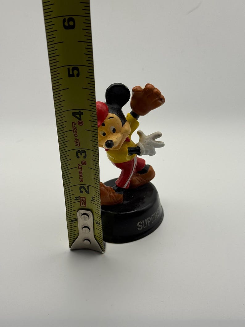 K&ouml;nnte beinhalten: Eine Mickey Mouse-Figur in Baseball-Uniform, etwa 7,6 cm hoch. Die Figur steht auf einem schwarzen Sockel mit dem Wort "SUPER". Mickey tr&auml;gt ein gelbes Hemd, eine rote Hose, eine rote M&uuml;tze und einen braunen Baseballhandschuh.