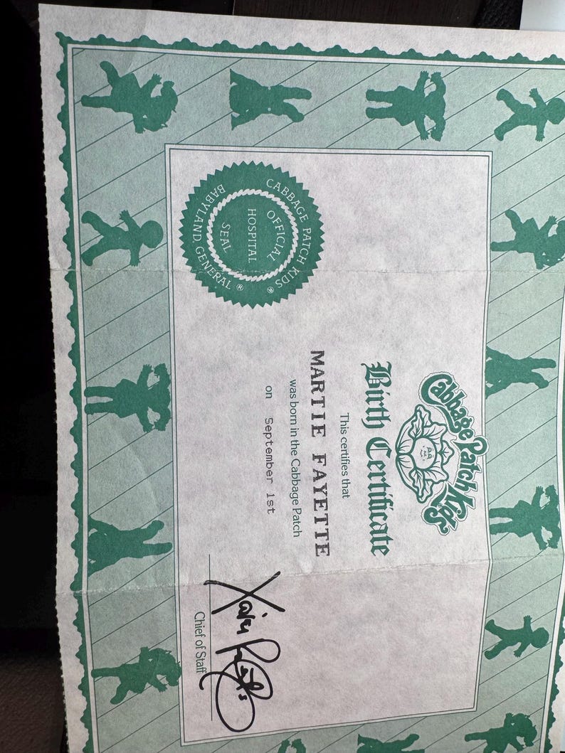 May include: A Cabbage Patch Kids birth certificate printed on light green paper with a dark green border featuring silhouettes of dolls. The document includes the text Birth Certificate, Martie Fayette, September 1st, and a signature.