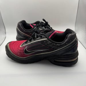 May include: Pair of black and red athletic shoes with a swoosh logo. The shoes have a black sole, black laces, and a pink accent around the ankle. The upper part of the shoe is a gradient of red to black.