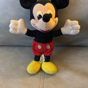 May include: A vintage plush Mickey Mouse toy with black fur, yellow shoes, and red shorts with white buttons.
