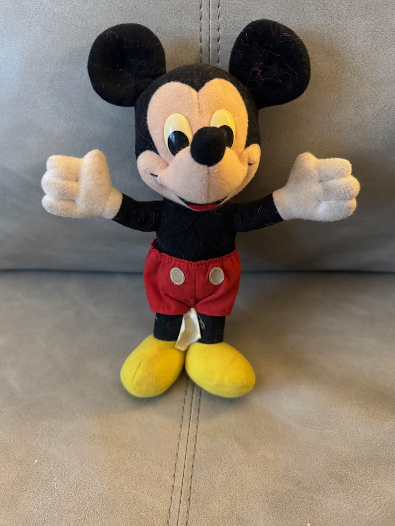 May include: A vintage plush Mickey Mouse toy with black fur, yellow shoes, and red shorts with white buttons.
