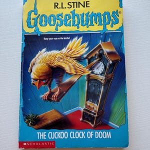 May include: A paperback book titled "Goosebumps: The Cuckoo Clock of Doom" by R.L. Stine. The cover features a yellow and brown bird perched on a wooden plank, with a grandfather clock and the text "Keep your eye on the birdie!"