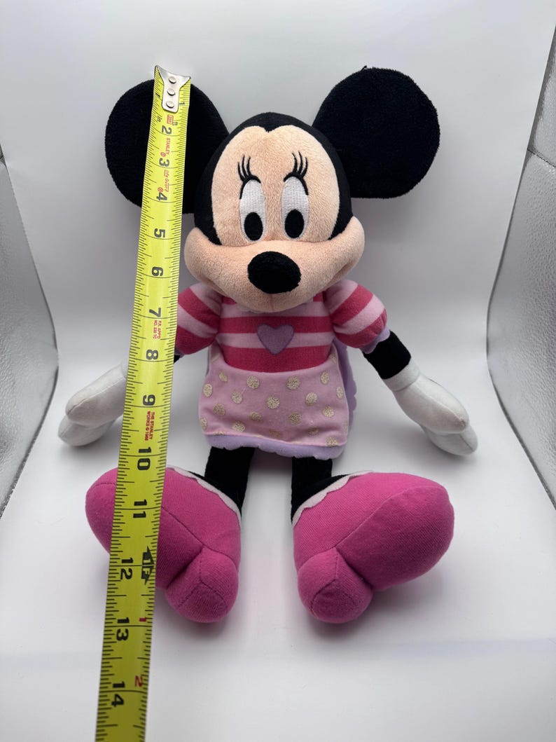 May include: A Minnie Mouse plush doll, approximately 14 inches tall, with black ears, a pink and white striped top, and pink polka-dotted skirt. The doll has large pink shoes and white gloves.