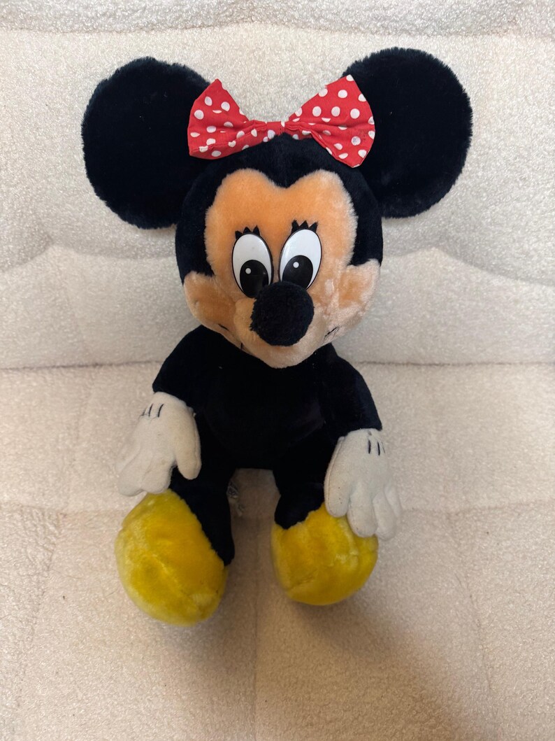 Puede incluir: Mu&ntilde;eca de peluche de Minnie Mouse con pelaje negro, orejas grandes y redondas y un lazo rojo con lunares blancos. La mu&ntilde;eca tiene una cara bronceada, guantes blancos y zapatos amarillos. Es un juguete infantil cl&aacute;sico.